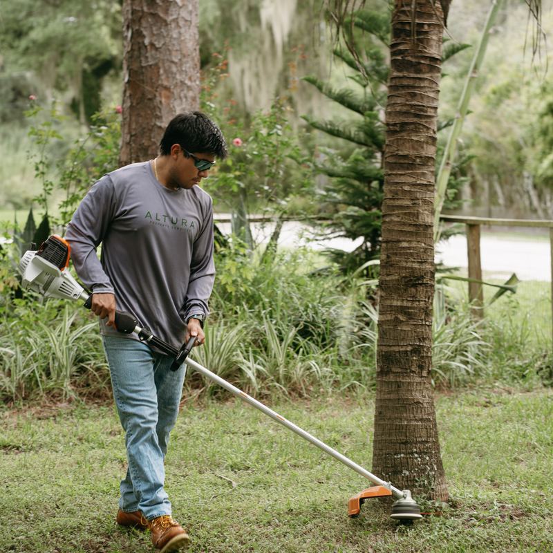 Altura Property Services crew member string trimming beside a palm tree